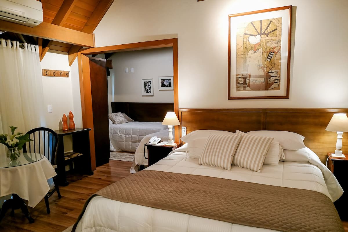 Una habitación de hotel con una cama grande, mesitas de noche con lámparas, una pequeña mesa con un florero y un cuadro en la pared.