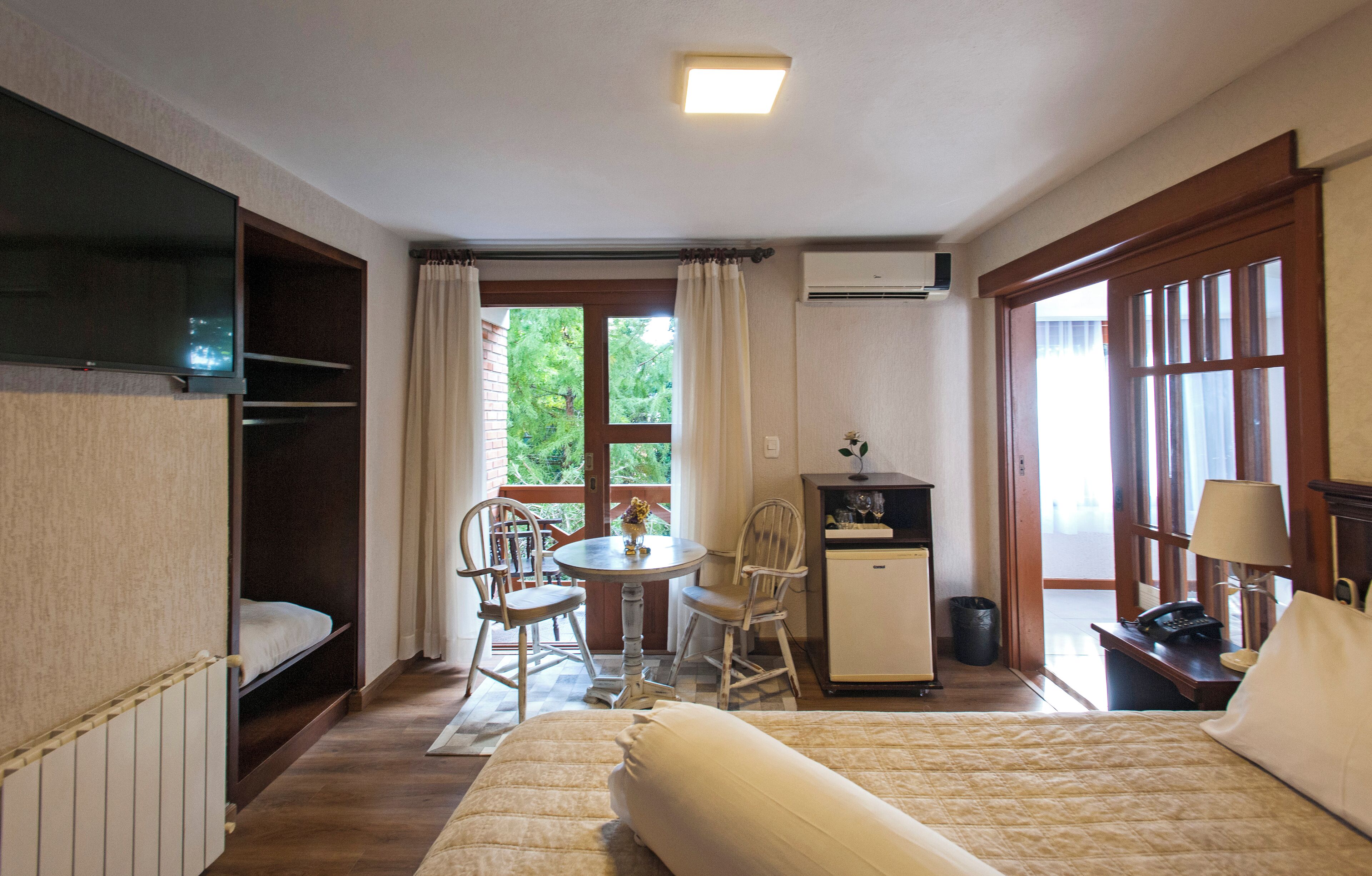 Habitación de hotel con cama, escritorio, silla, mesita pequeña, televisor y ventana con cortinas.