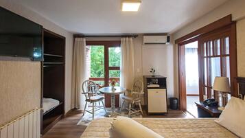 Habitación de hotel con cama, escritorio, silla, mesita pequeña, televisor y ventana con cortinas.