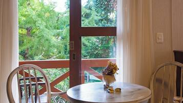A round table with a vase of flowers and chocolates, two chairs, and a view of greenery through a window.