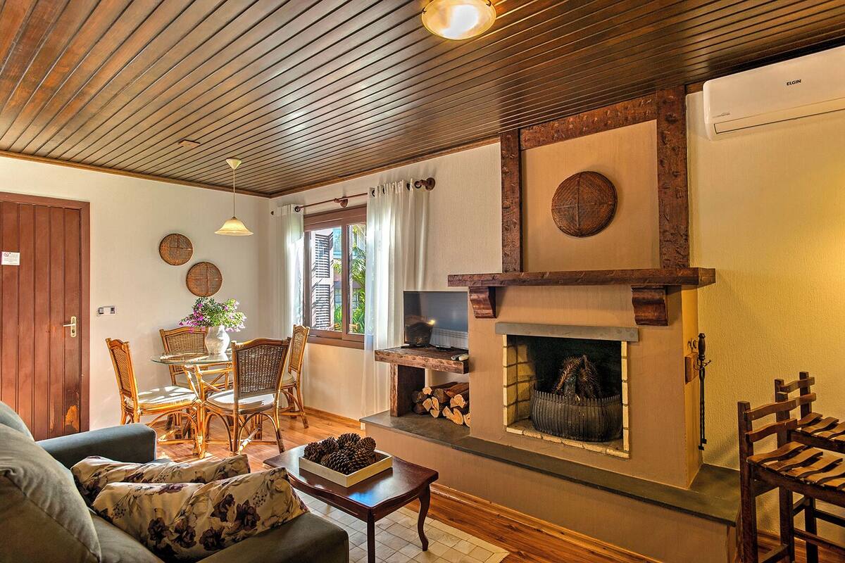 Una sala de estar acogedora con chimenea, techo de madera y un comedor con mobiliario de mimbre.