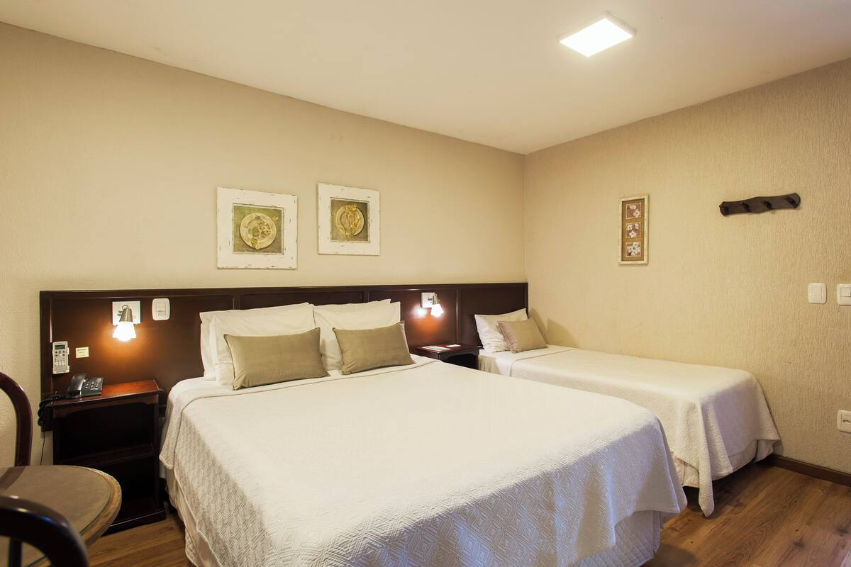 Habitación de hotel con dos camas, un escritorio y una silla. Luces fijadas en la pared y cuadros enmarcados.