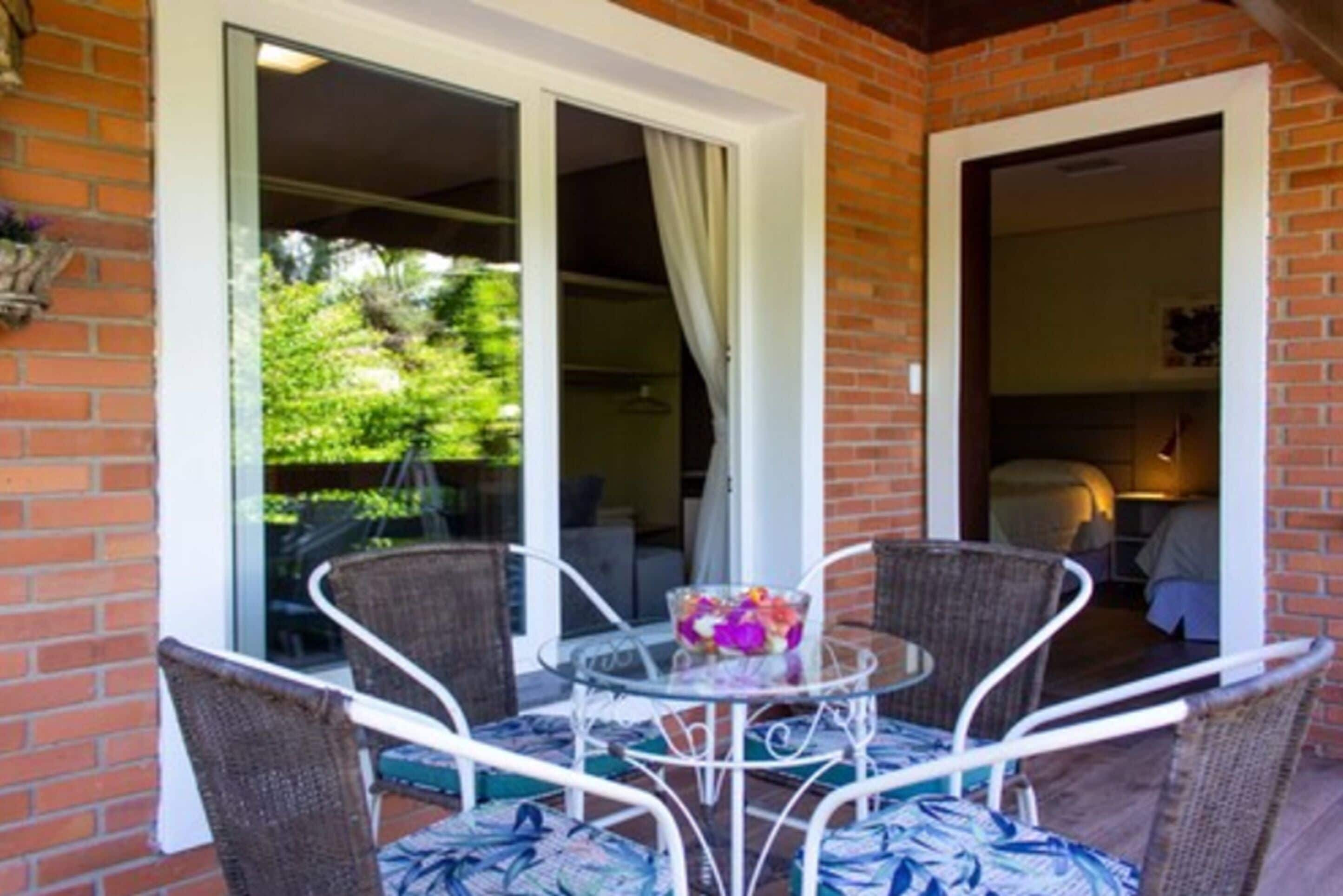 A patio with wicker chairs and a glass table, a brick wall, and a glass door leading to a garden.