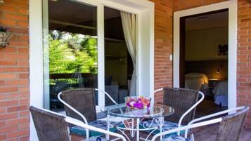 A patio with wicker chairs and a glass table, a brick wall, and a glass door leading to a garden.