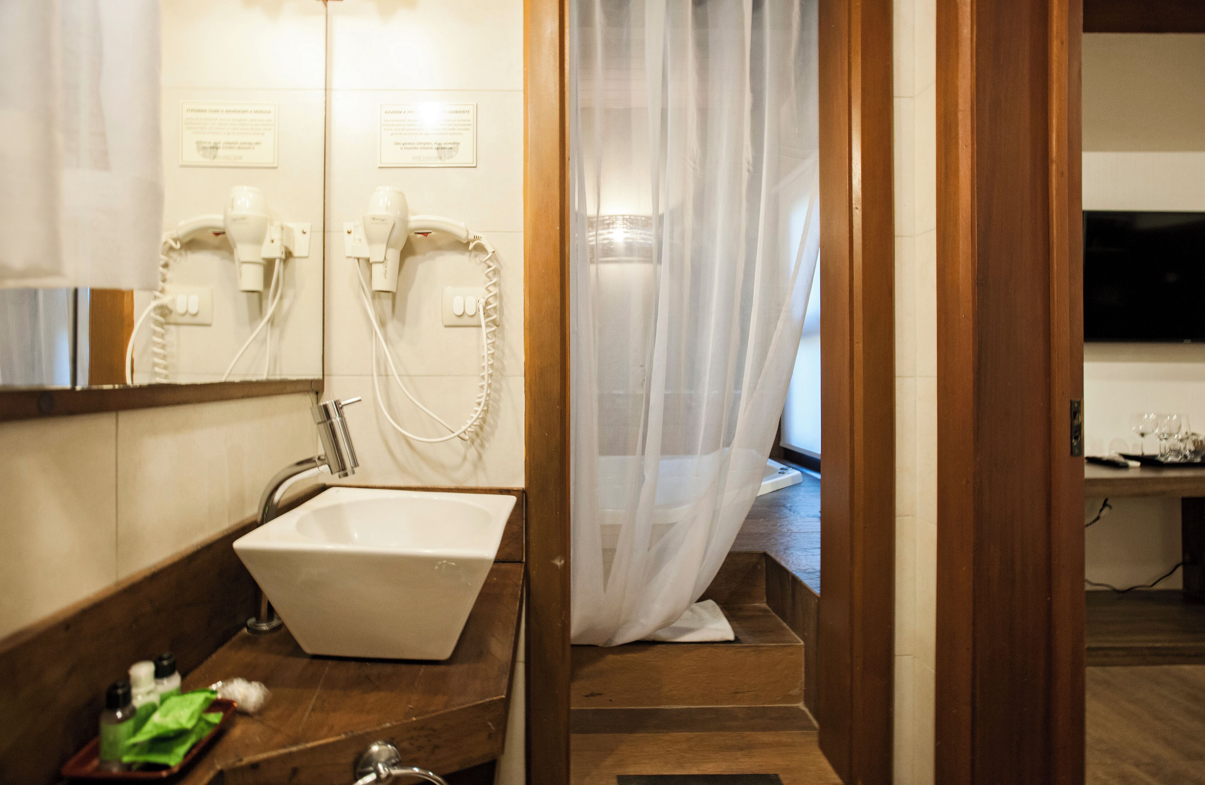 A bathroom with a sink, mirror, hairdryer, and shower curtain.