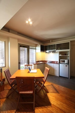 A compact kitchen with a dining area, wooden chairs, a table, and a microwave.