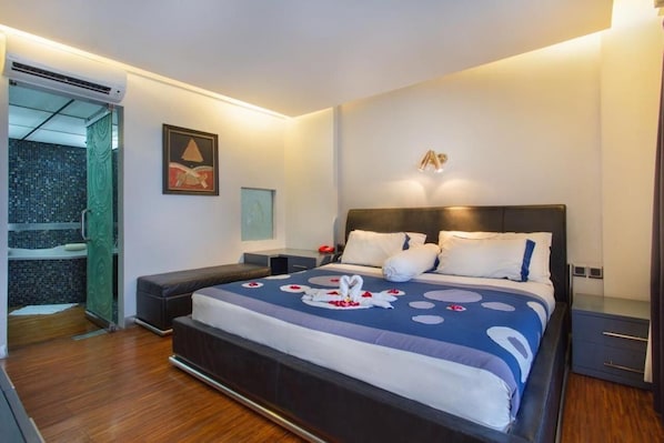 A modern hotel room with a large bed, a bedside table, a nightstand, and a bathroom with a shower and a tiled wall.