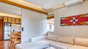 A modern living room with a sectional sofa, a wooden coffee table, and a kitchen area with a microwave and refrigerator.