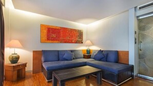 A modern living room with a sectional sofa, two side tables with lamps, a coffee table, and a large abstract painting on the wall. - Sejuk Suites (Legian)