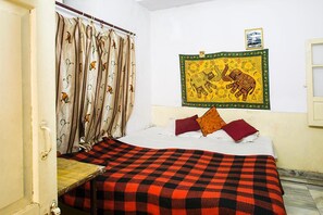 A room with a bed, a checkered blanket, curtains with a floral pattern, and a framed picture on the wall. - Kunwar Haveli (Udaipur)