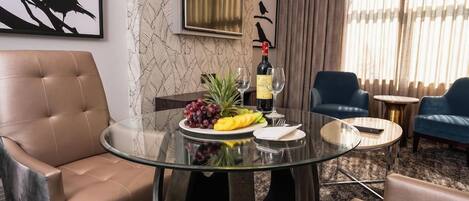 A room with a glass-top table, two leather chairs, a bottle of wine, and a plate of fruit.