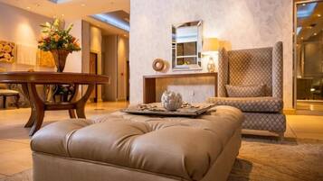 A modern lobby with a leather ottoman, a wooden side table, and a patterned armchair.