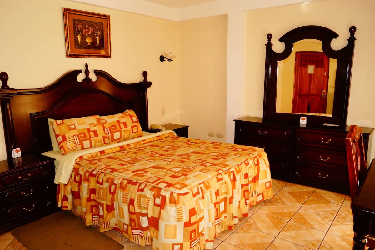 A bedroom with a wooden bed, a nightstand, a dresser, and a mirror.
