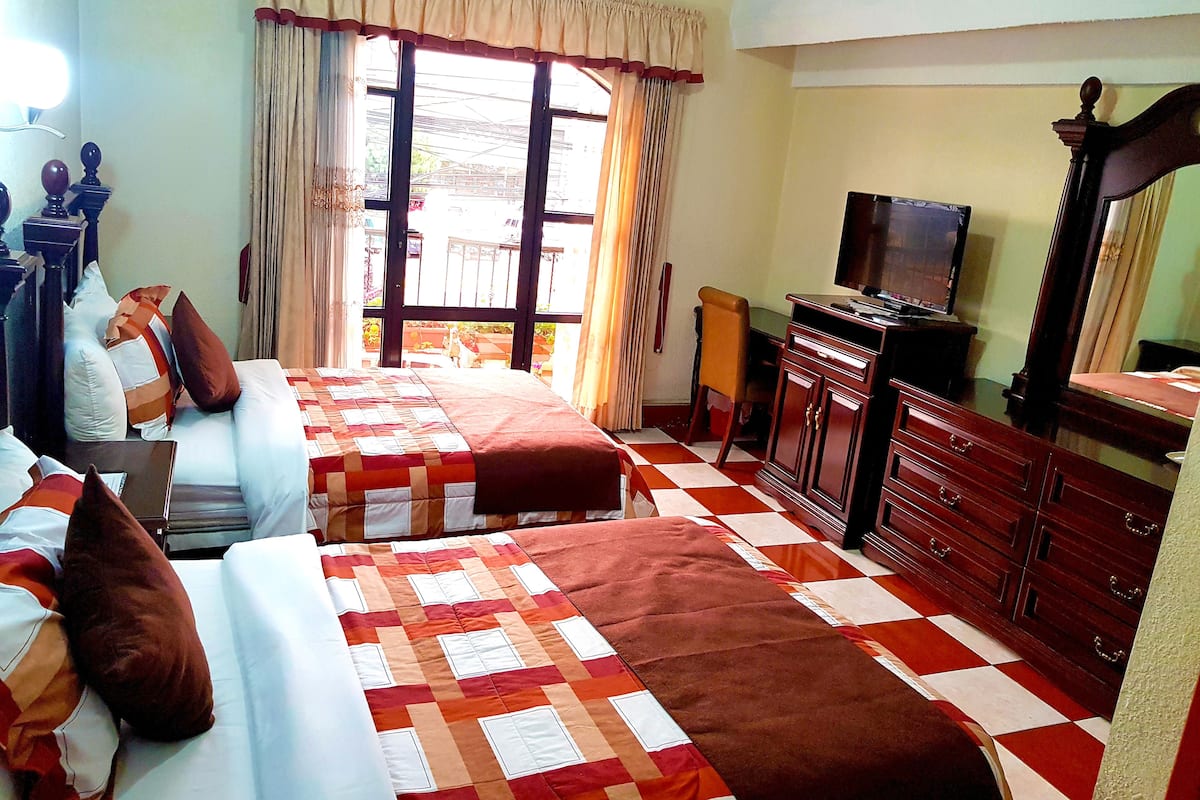 A hotel room with two beds, a television, a dresser, and a window with curtains.
