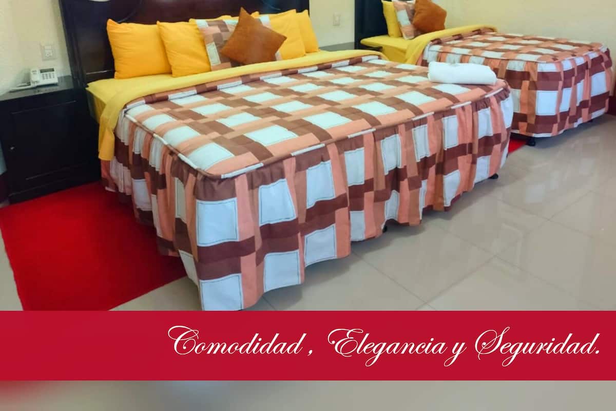 A hotel room with two beds, each with a checkered bedspread and yellow pillows. The room has a red carpet and a wooden headboard. There is a framed picture on the wall and a telephone on the nightstand.