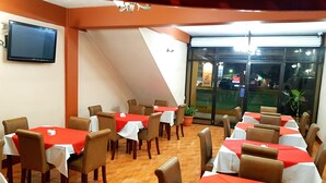 Un restaurant doté de nombreuses tables et chaises, d’un téléviseur à écran plat fixé au mur et offrant une vue sur la rue.