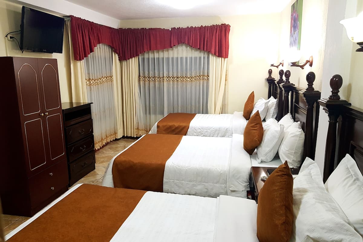 A hotel room with two beds, a wardrobe, a television, curtains, and a chandelier.