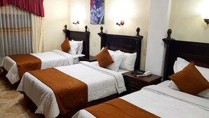 Une chambre d’hôtel avec trois lits, chacun doté de draps blancs et d’oreillers décoratifs marron. On y trouve des têtes de lit en bois, une table de chevet avec un téléphone et un tableau accroché au mur.