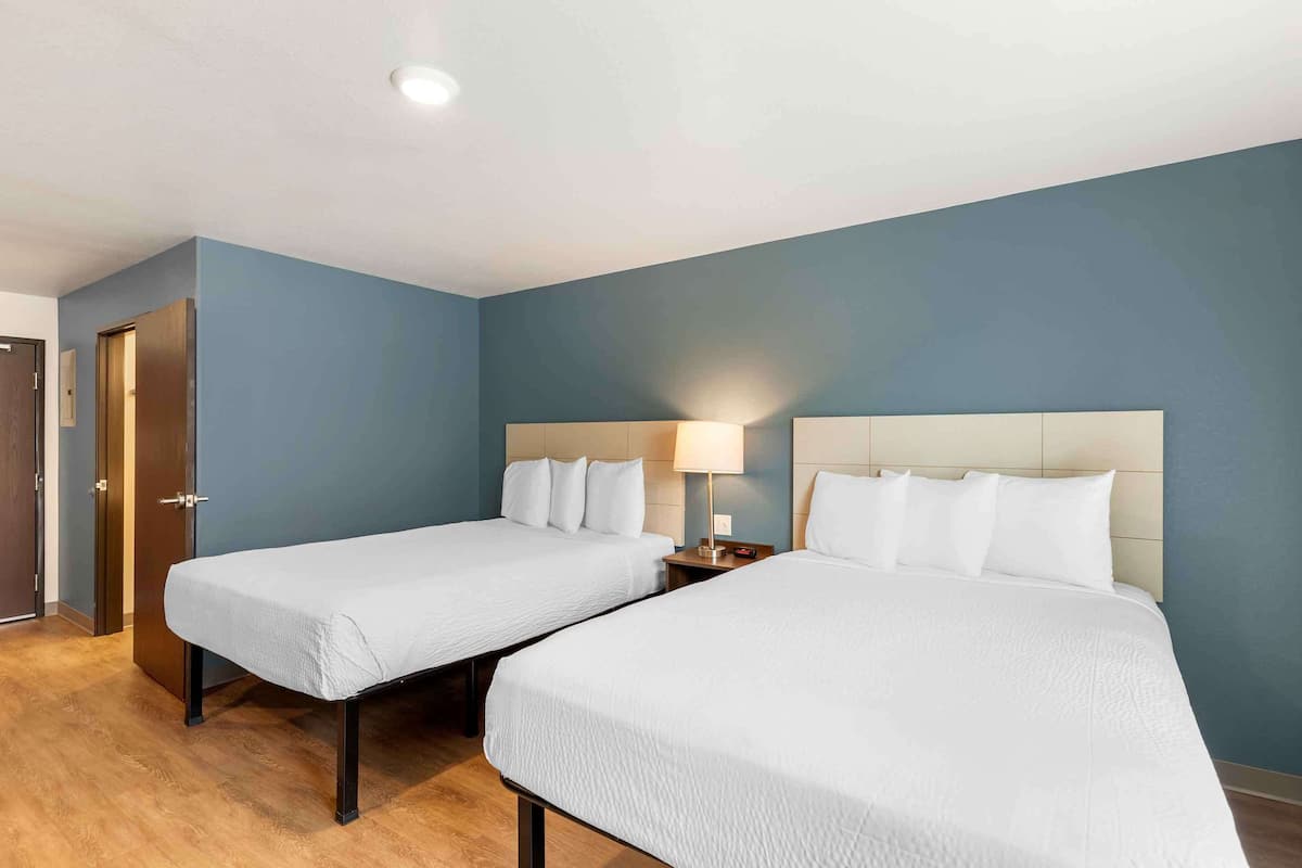 Une chambre d’hôtel avec deux lits simples, un plancher en bois et un mur d’accent bleu.