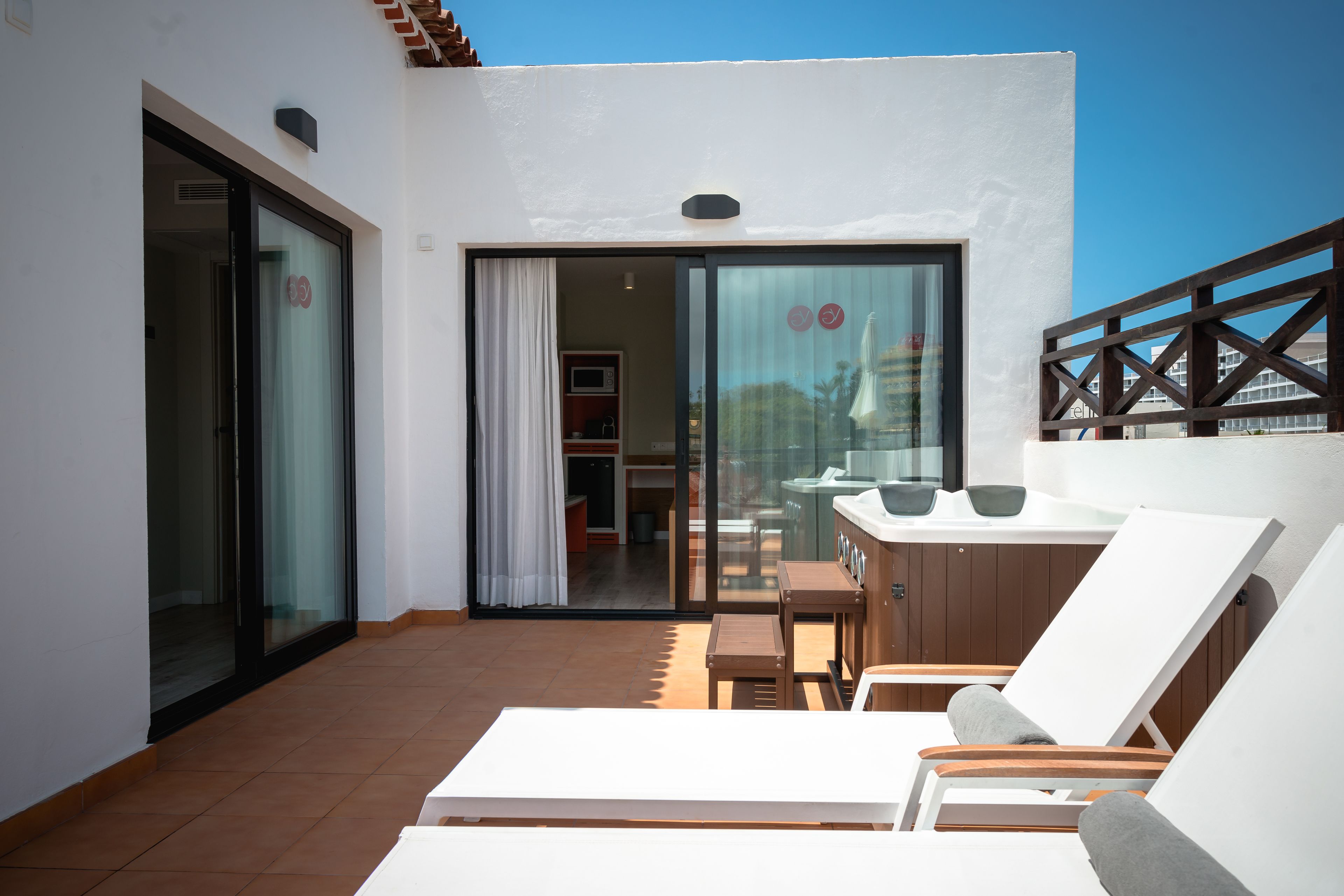 Un balcón con una mesa y sillas, un ventanal corredero y vistas al exterior.