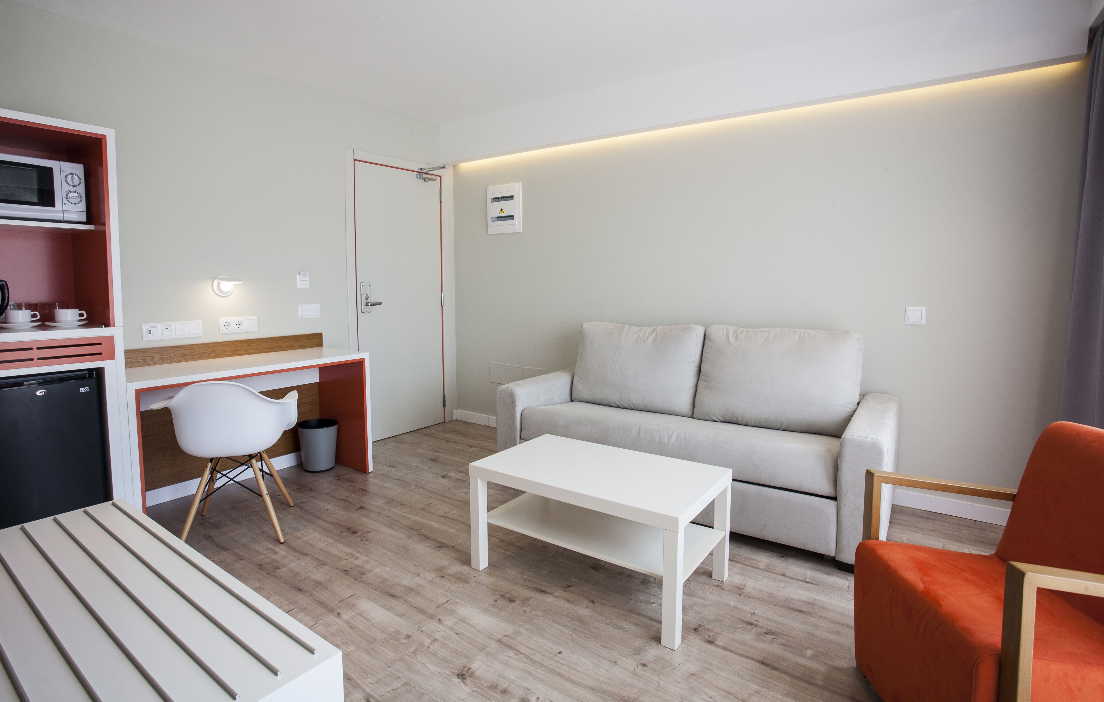 A modern, compact living space with a kitchenette, a sofa, a dining table, and a bright, well-lit room.