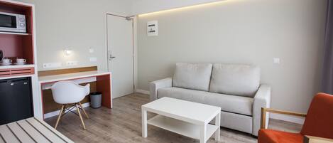 A modern, compact living space with a kitchenette, a sofa, a dining table, and a bright, well-lit room.