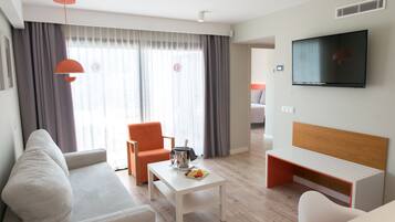 Habitación de hotel moderna con sofá, sillón, una mesa de centro con fruta, televisor y vistas amplias por grandes ventanales.