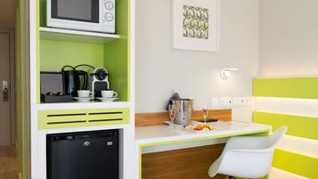 A compact kitchenette with a microwave, coffee maker, and small refrigerator. A dining area with a white chair and a table is visible.
