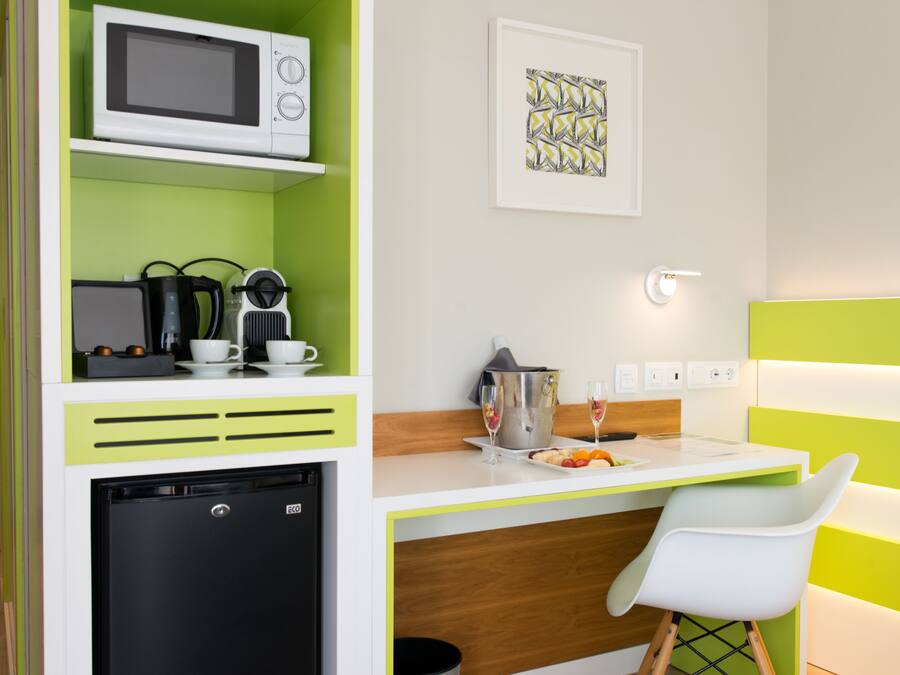 A compact kitchenette with a microwave, coffee maker, and small refrigerator. A dining area with a white chair and a table is visible.