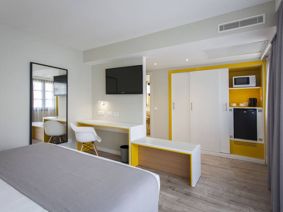Une chambre d’hôtel équipée d’un lit, d’un bureau, d’une chaise, d’une télévision, d’un four à micro-ondes et d’une armoire.
