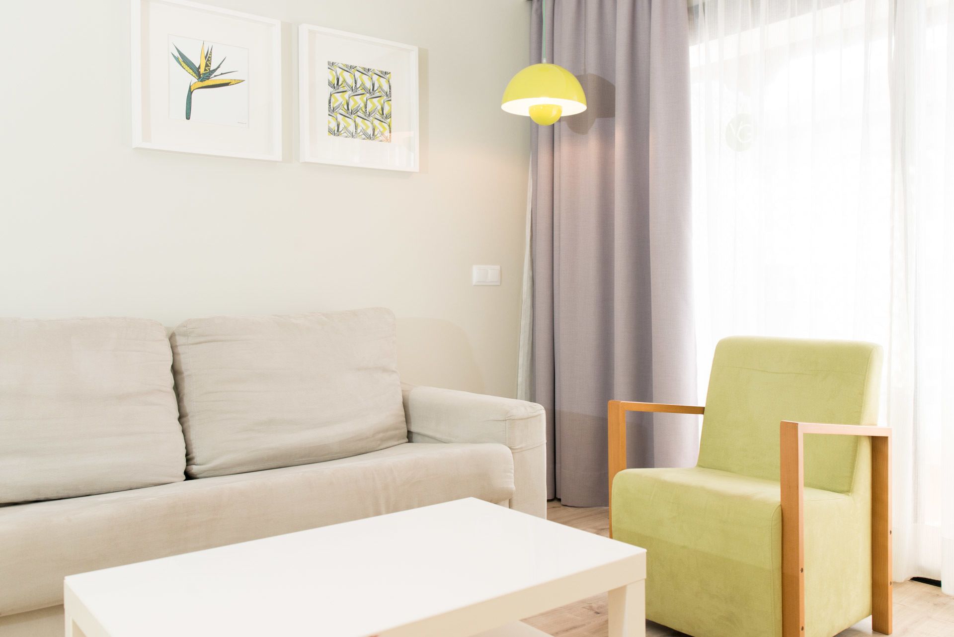 Un salon avec un canapé, un fauteuil vert, une table basse blanche et deux tableaux encadrés accrochés au mur.
