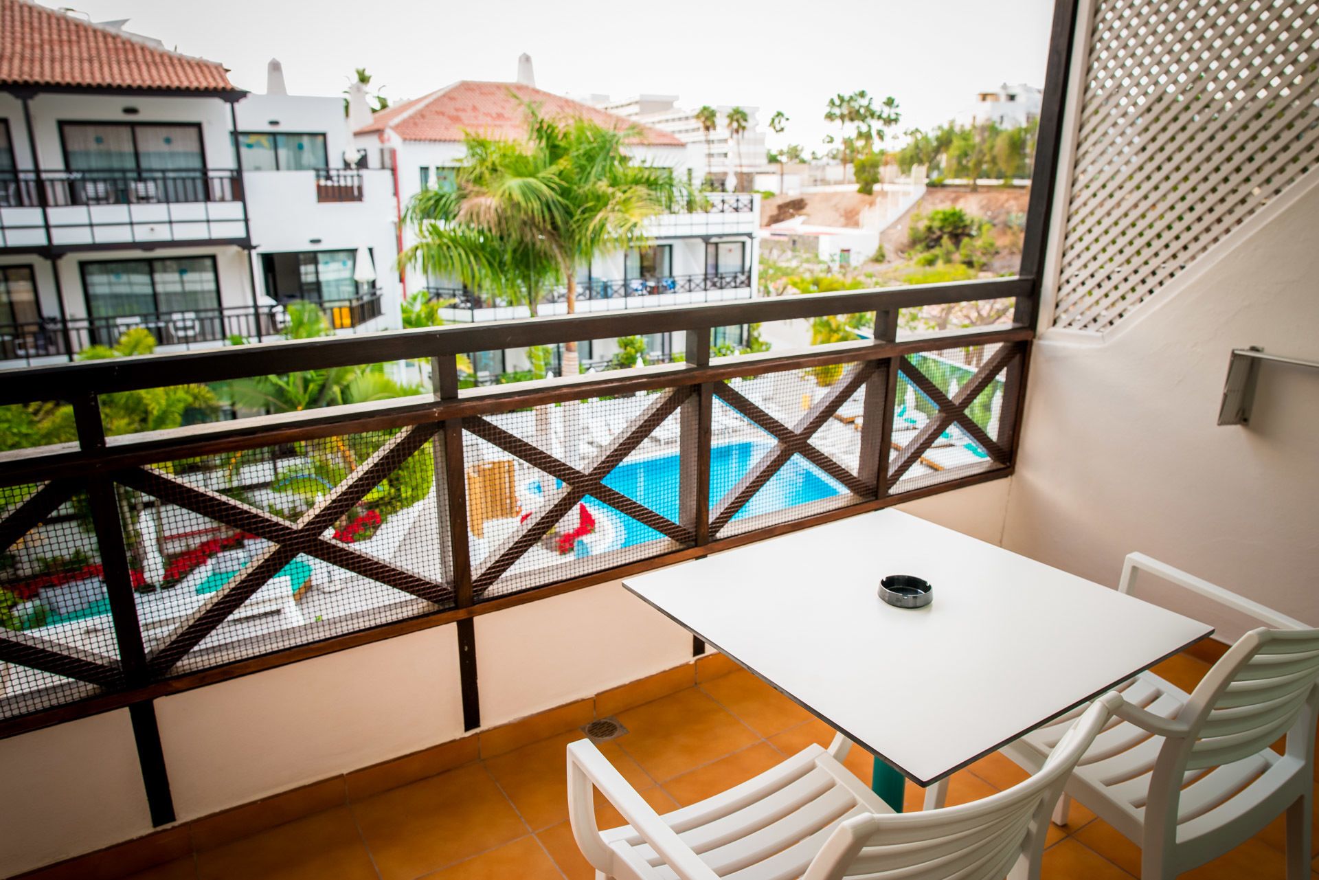 Un balcon donnant sur une piscine, avec des chaises blanches et une table blanche.