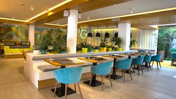 A modern restaurant with a long counter, blue chairs, and potted plants.