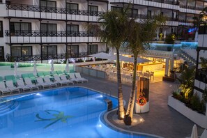 Zona de piscina de hotel con una piscina grande, sillas de descanso y un área de bar.