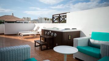 Una terrazza sul tetto con idromassaggio, mobili in vimini e vista sullo skyline della città.