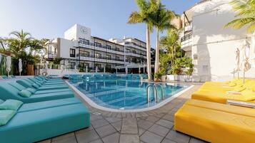 A swimming pool with lounge chairs, a building with balconies, and palm trees.