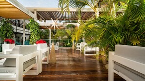 A covered outdoor seating area with wooden flooring, white lounge chairs, and tropical plants. - Vanilla Garden Boutique Hotel - Adults Only (Arona)