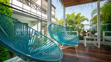 Un espacio al aire libre techado con dos sillas turquesas, una terraza de madera y una barandilla blanca.