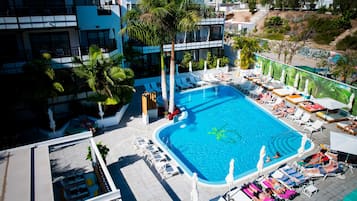 Una piscina en la azotea con tumbonas y sombrillas, rodeada de palmeras y edificios modernos.