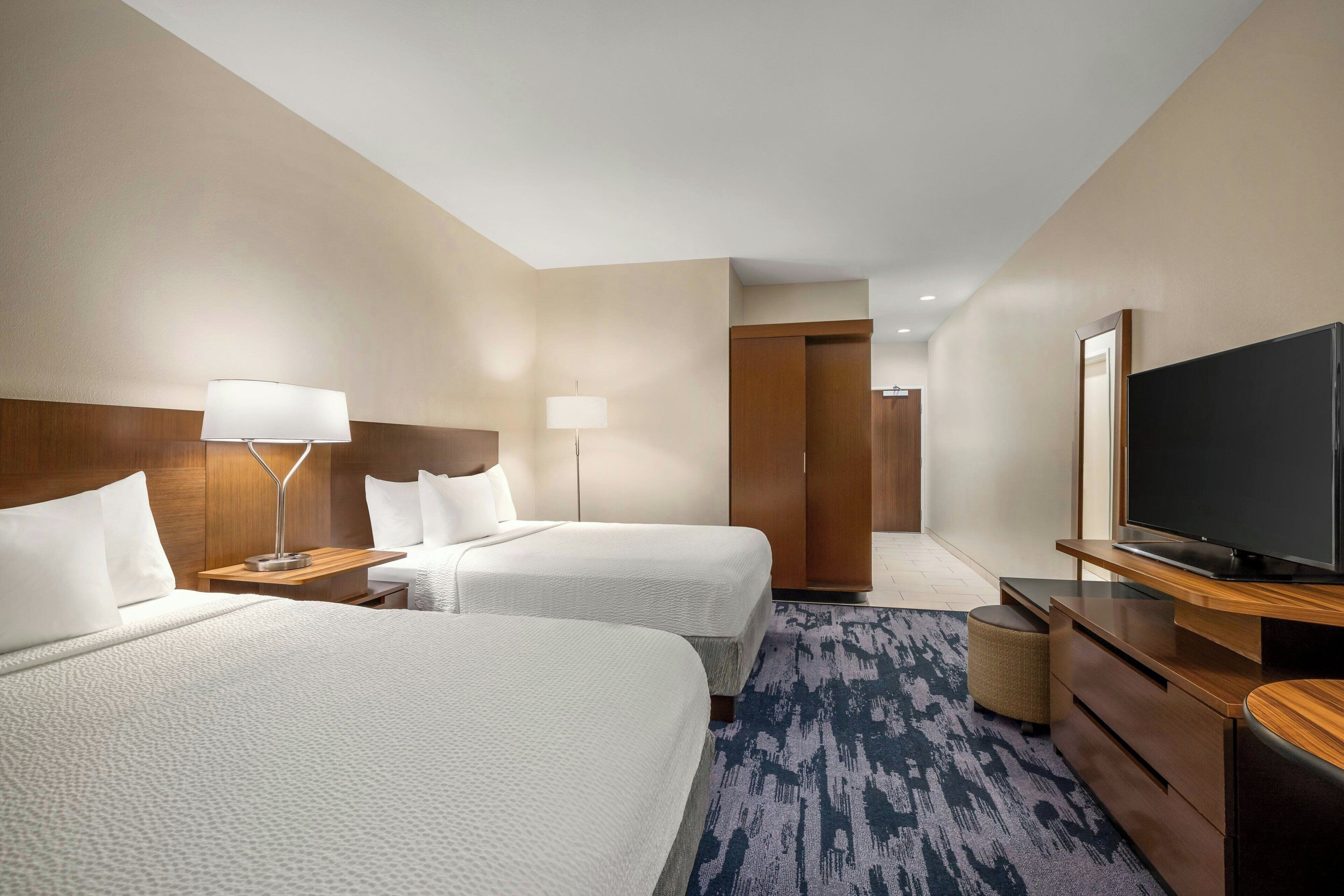 A hotel room with two beds, a flat-screen TV, a desk, and a lamp.