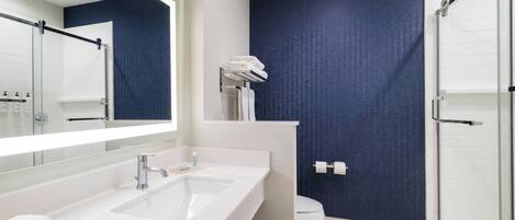 Un baño moderno con un lavamanos blanco, un espejo grande, una ducha y una pared azul oscuro con textura.