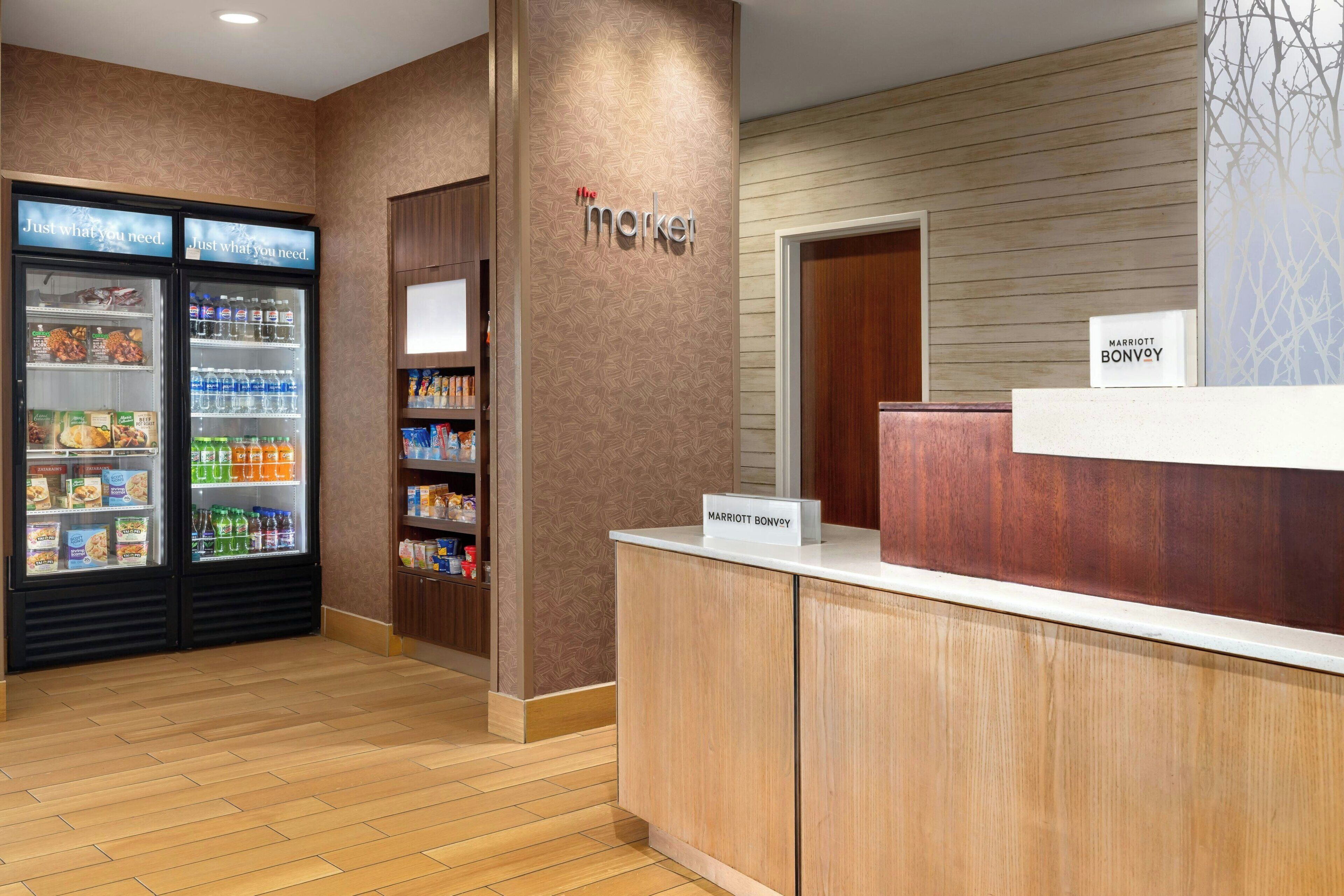 A hotel reception area with a 'Market' sign, a refrigerated display case with snacks and beverages, and a 'Marriott Bonvoy' sign on the counter.