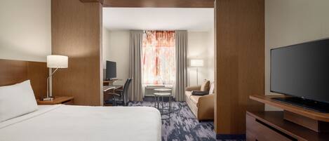 Habitación de hotel con una cama grande, un escritorio con silla, un sofá, un televisor y una ventana con cortinas.