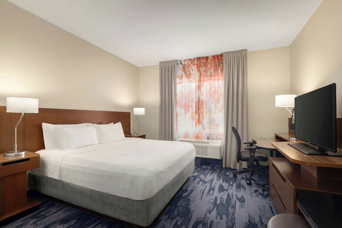 A hotel room with a large bed, a desk with a computer, a TV, and a window with curtains.