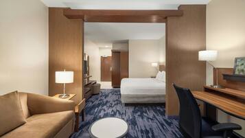 A hotel room with a bed, a desk, a chair, a round table, a sofa, and a lamp.