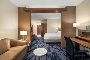 A hotel room with a bed, a desk, a chair, a round table, a sofa, and a lamp.