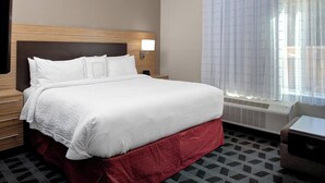 A hotel room with a large bed, a bedside table, a lamp, and a window with curtains. - TownePlace Suites by Marriott Albany (Albany)
