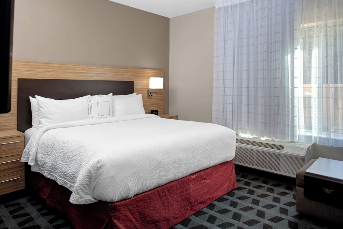 A hotel room with a large bed, a bedside table, a lamp, and a window with curtains.