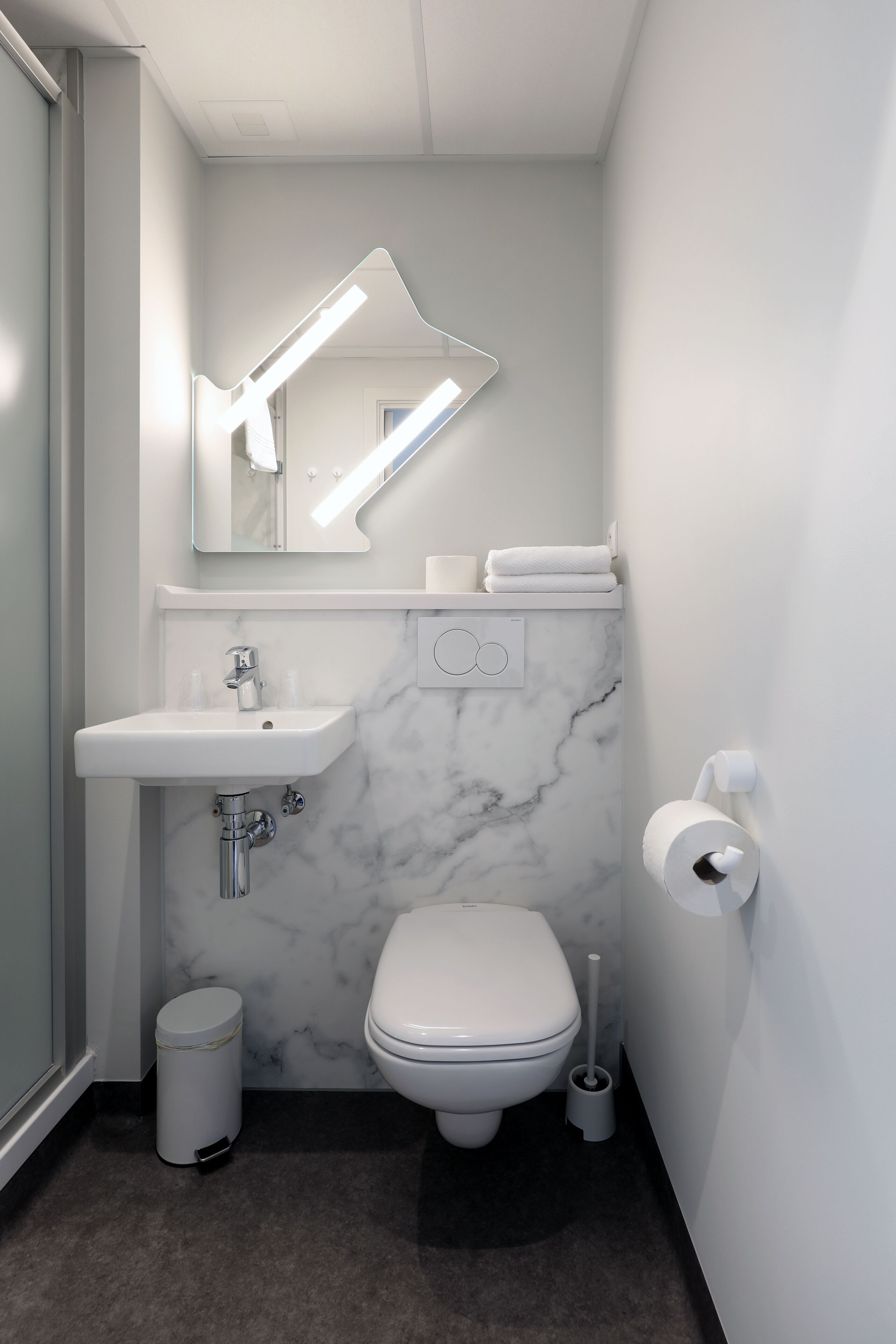 A modern bathroom with a marble sink, a toilet, a trash can, and a toilet paper holder.