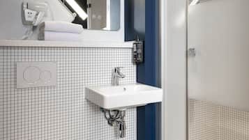 Une salle de bain moderne avec des toilettes blanches, un lavabo, un miroir et une douche.